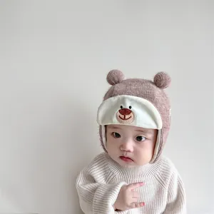 Detail of pink knitted baby trapper hat with embroidered bear face and dual pom-poms