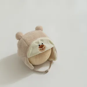 Detailed view of beige knit baby trapper hat with bear embroidery and plush lining
