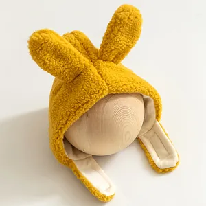 Detail einer hellgelben Baby-Plüschmütze mit Hasenohren auf einem Holzmodell für den Winter