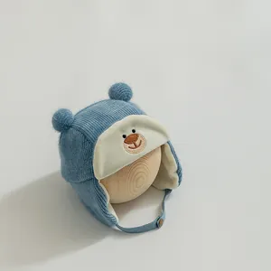 Detailed close-up of blue knit baby bear hat with fluffy pom-poms and earflaps