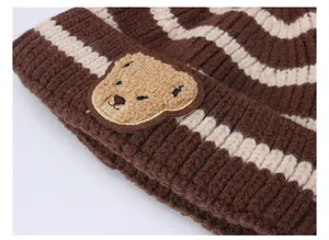 Dettaglio di un cappello lavorato a maglia a righe marroni con simpatico orsetto
