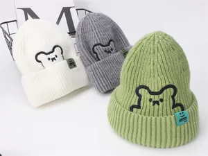 Dettaglio di cappelli invernali in maglia bianco, grigio e verde con ricamo a orso