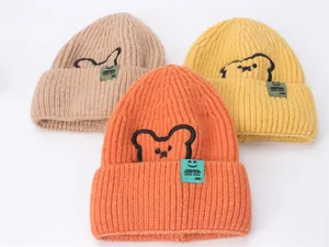 Dettaglio di tre berretti in maglia kaki, arancione e giallo con ricamo a forma di orso
