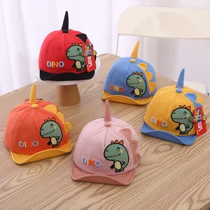 Detail view of five colorful cotton baby dinosaur baseball caps on a wooden table