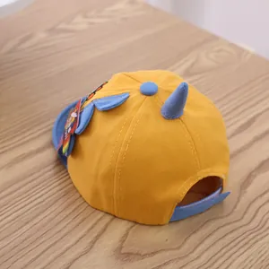 Detailed view of yellow cotton baby hat with blue dinosaur horns and adjustable strap