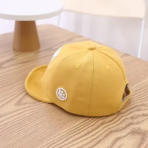 Détail de la casquette bébé en coton jaune avec broderie patte blanche sur table en bois