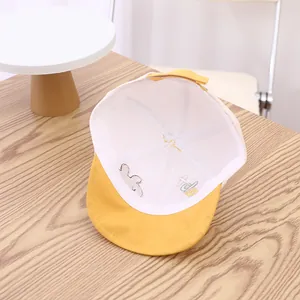 Détail de la casquette bébé avec broderie lapin et visière jaune sur fond en bois