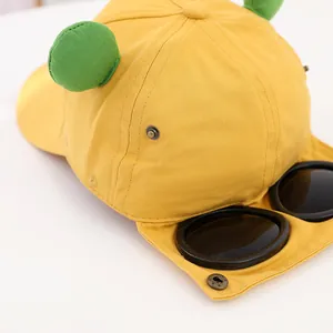 Detailansicht der gelben Baseballkappe mit grünen Ohren und markanter Brille