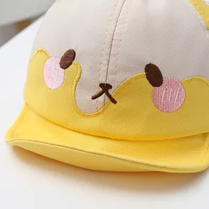 Detailaufnahme der Bären-Stickerei auf einer gelb-weißen Baby-Baseballkappe aus Baumwolle