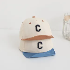 Dettaglio dei cappellini da baseball beige per neonati con patchwork blu e marrone e C