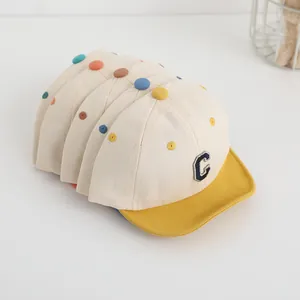Dettaglio del cappellino da neonato con visiera morbida, pompon colorati e ricamo della lettera C