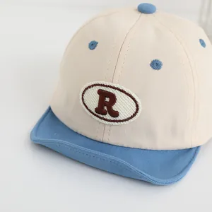 Dettaglio del cappellino da neonato con ricamo R, visiera blu e tessuto in cotone bianco