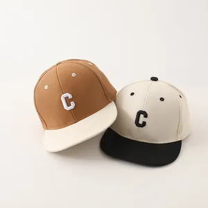 Detail van tweekleurige kinderpetten met C-letter borduursel in bruin en gebroken wit