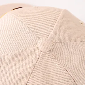 Dettaglio della corona del cappellino in cotone beige con bottone e cuciture a sei pannelli