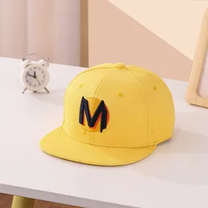 Dettaglio del cappellino snapback giallo con lettera M ricamata e trama in cotone