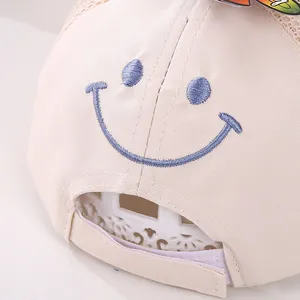 Close-up of beige baby mesh baseball cap showing blue smiley face embroidery and adjustable strap