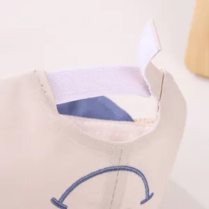 Detail view of the adjustable white Velcro strap on the beige cotton baby baseball cap