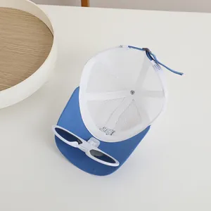 Detail of blue and white mesh baseball cap featuring decorative white sunglasses on the brim