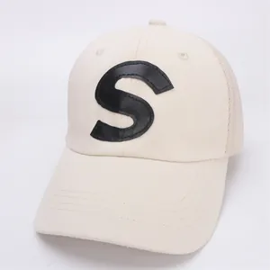Close-up of beige mesh baseball cap featuring a black leather S letter patch and brim stitching