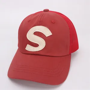 Detail of red mesh trucker hat featuring a cream leather letter S patch and curved brim