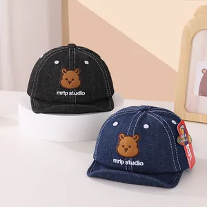 Détail de la broderie ours et texture denim sur des casquettes souples pour bébés