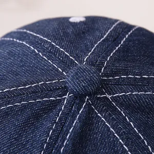Détail du haut d'une casquette en jean pour bébé avec tissu bleu et coutures blanches