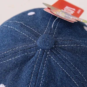 Dettaglio del cappello in denim blu per neonati con cuciture bianche e ricamo a puntini