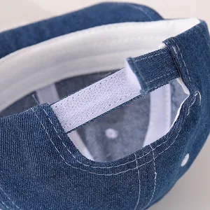 Dettaglio cappellino bimbo in denim blu con cinturino in velcro e cuciture bianche