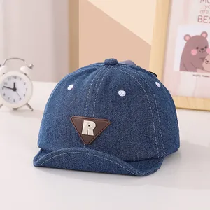 Dettaglio cappellino neonato in denim con etichetta R in pelle e visiera morbida