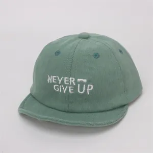 Detalle de textura de pana verde en gorra de bebé con bordado NEVER GIVE UP