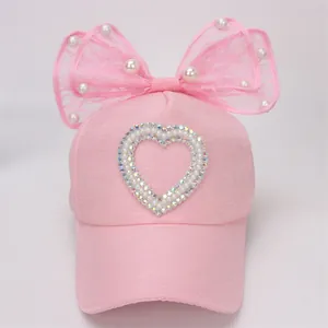 Detalle de gorra rosa para niña con lazo de encaje, perlas y un corazón de cristal