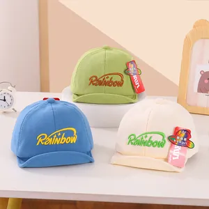 Detailed view of soft-brim baby baseball caps in green, blue, and cream with Rainbow embroidery
