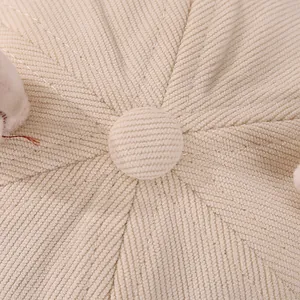 Macro view showing the soft corduroy texture and stitched button detail of the baby cap