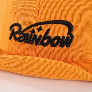 Close-up of orange baby baseball cap featuring black Rainbow embroidery and knit texture