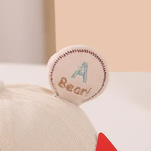 Detail of baby knit hat showing soft cream fabric with embroidered blue letter A Bear patch