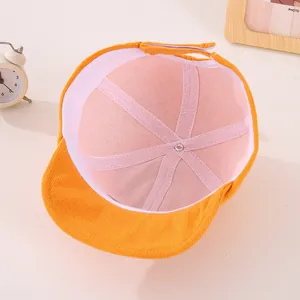 Detail view of orange corduroy baby cap lining with adjustable velcro strap and tag