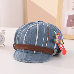 Détail d'une casquette rayée en jean pour bébé avec lanière marron sur surface blanche