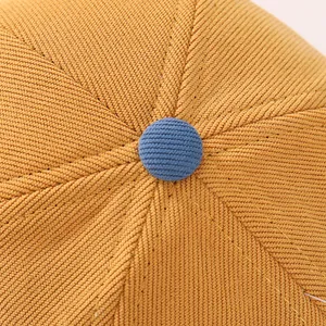 Dettaglio macro del cappello giallo per bambini con bottone blu e fili metallici