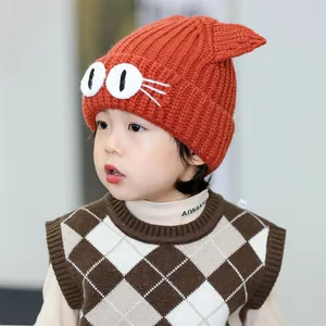 Detail view of bright orange knitted baby hat with cute cat ears and cartoon eyes