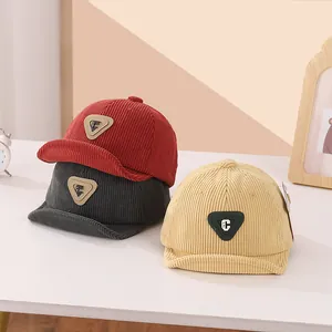 Close-up of three corduroy baby baseball caps with leather C patch in red, grey and beige