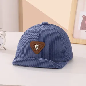 Detail showing blue corduroy fabric texture and triangle C-letter patch on baby cap