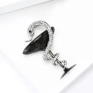 Détail d'une broche serpent en argent avec strass enroulée autour d'un verre à martini noir