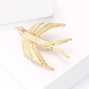 Golden swallow bird brooch with detailed feather texture on minimalist white platform