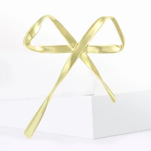 Élégante broche nœud doré mat aux lignes fluides sur support géométrique blanc