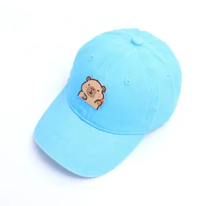 Detalle de gorra infantil de algodón azul claro con parche de carpincho de dibujos animados