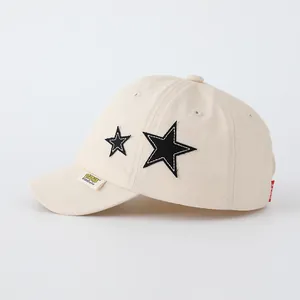 Detail of cream baseball cap with black star patches and yellow woven brand label