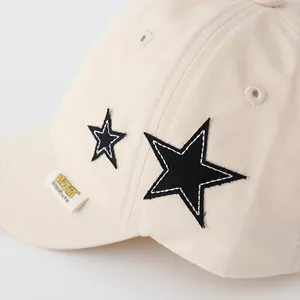 Close-up of beige cotton baseball cap with black star patches and fabric label detail