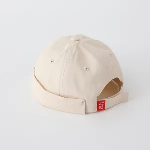 Detail of adjustable strap and red brand tag on a cream-colored cotton docker hat for kids