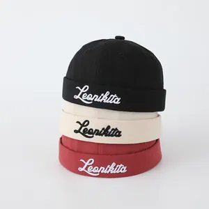 Detalle de gorros docker de algodón apilados en negro, beige y rojo con bordado fino