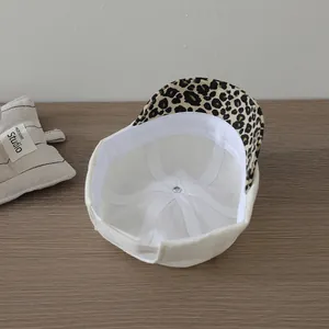 Toddler white docker hat with leopard print brim on a dark wood grain surface